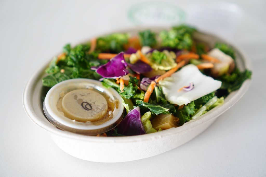 Colorful healthy salad with kale, cabbage, and carrots, featuring dressing for added flavor.