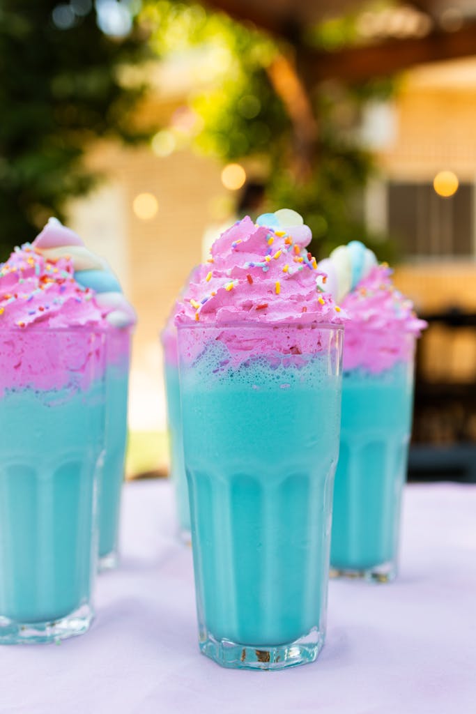 Colorful unicorn-themed milkshakes with bright pink and blue whipped cream in tall glasses.