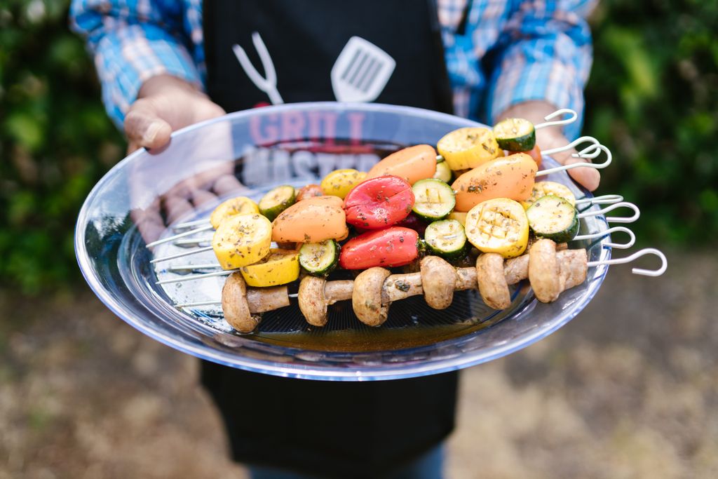 Colorful vegetable skewers being presented at an outdoor barbecue setting.