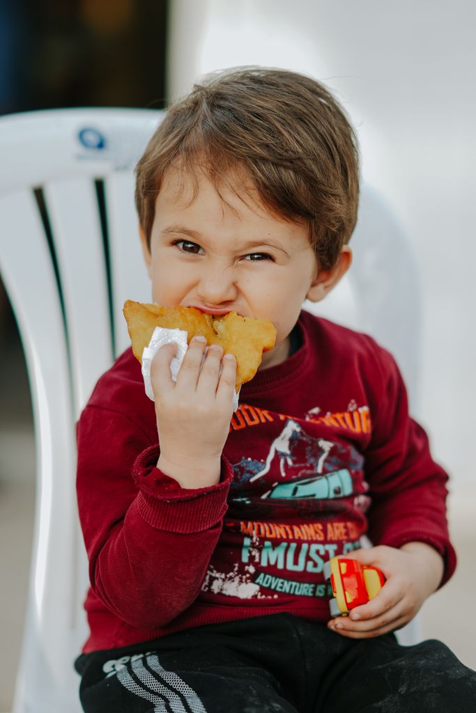 Cute child biting into a crispy snack while sitting outdoors on a sunny day.