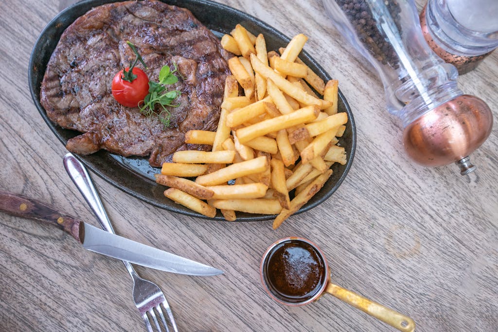 Delicious grilled steak with fries, tomato, and garnish on a wooden table, elegantly presented for lunch or dinner.