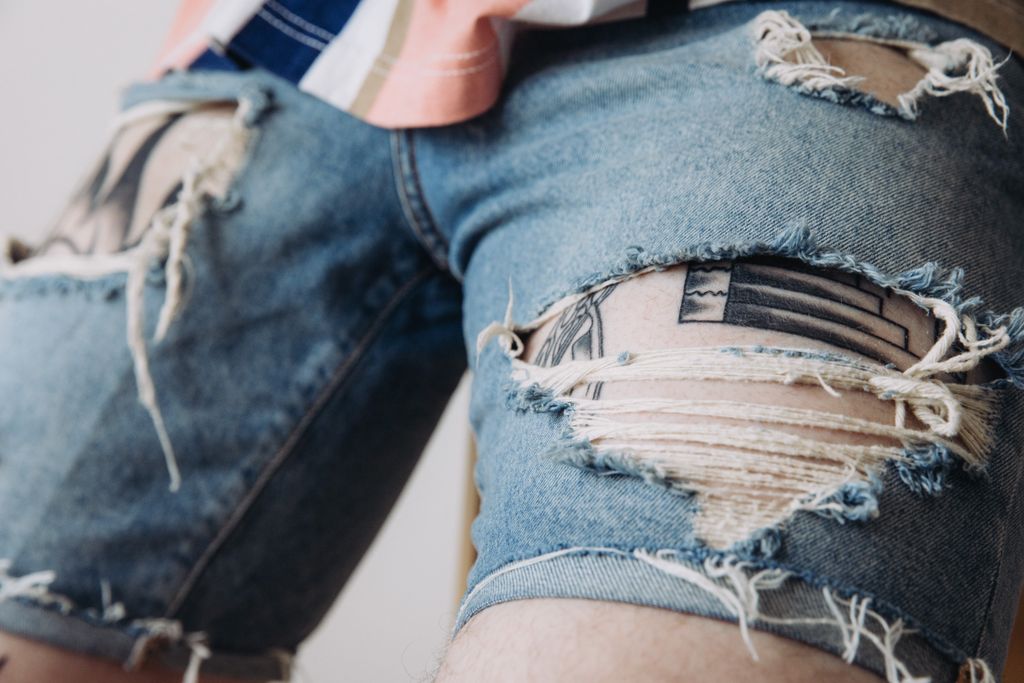 Detailed view of worn denim shorts with tattoos peeking through, showcasing unique style.