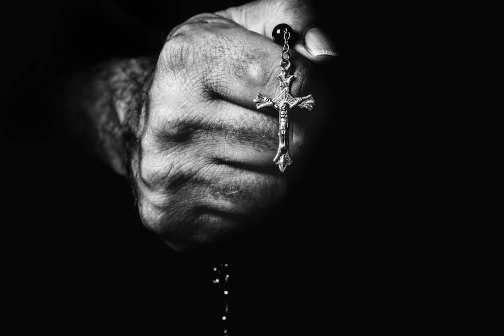 Dramatic black and white close-up of a hand holding a rosary cross.