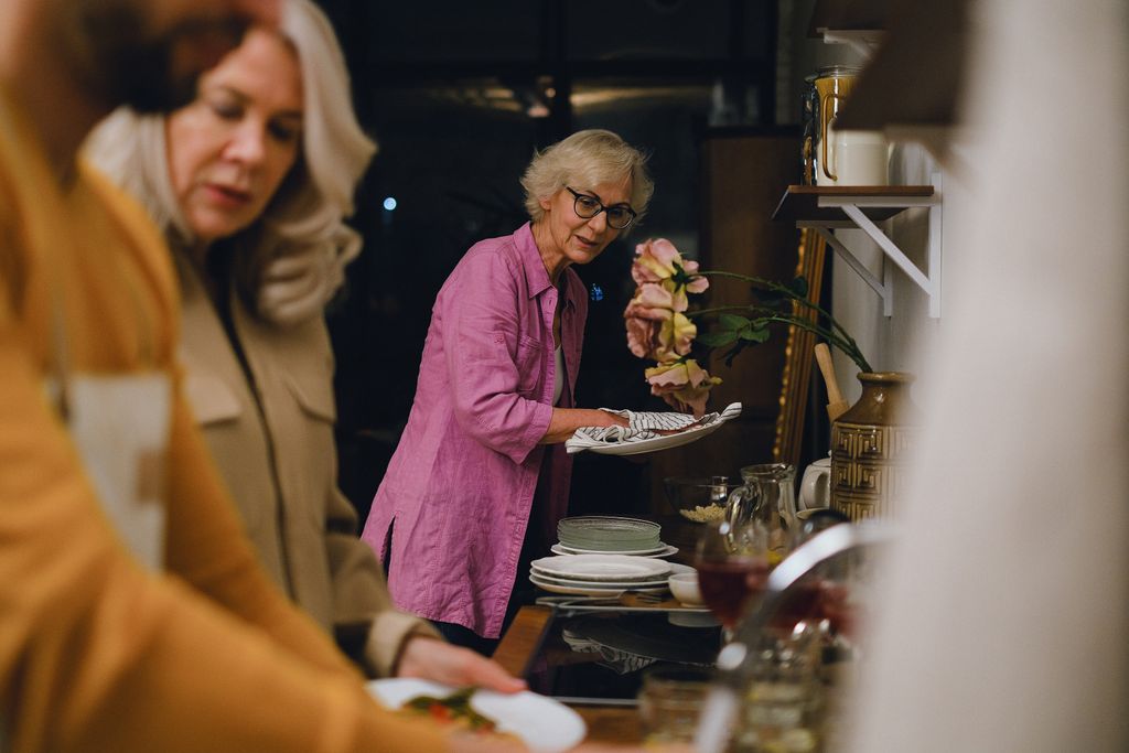 Elderly woman tidying dishes in a warm, home kitchen setting.