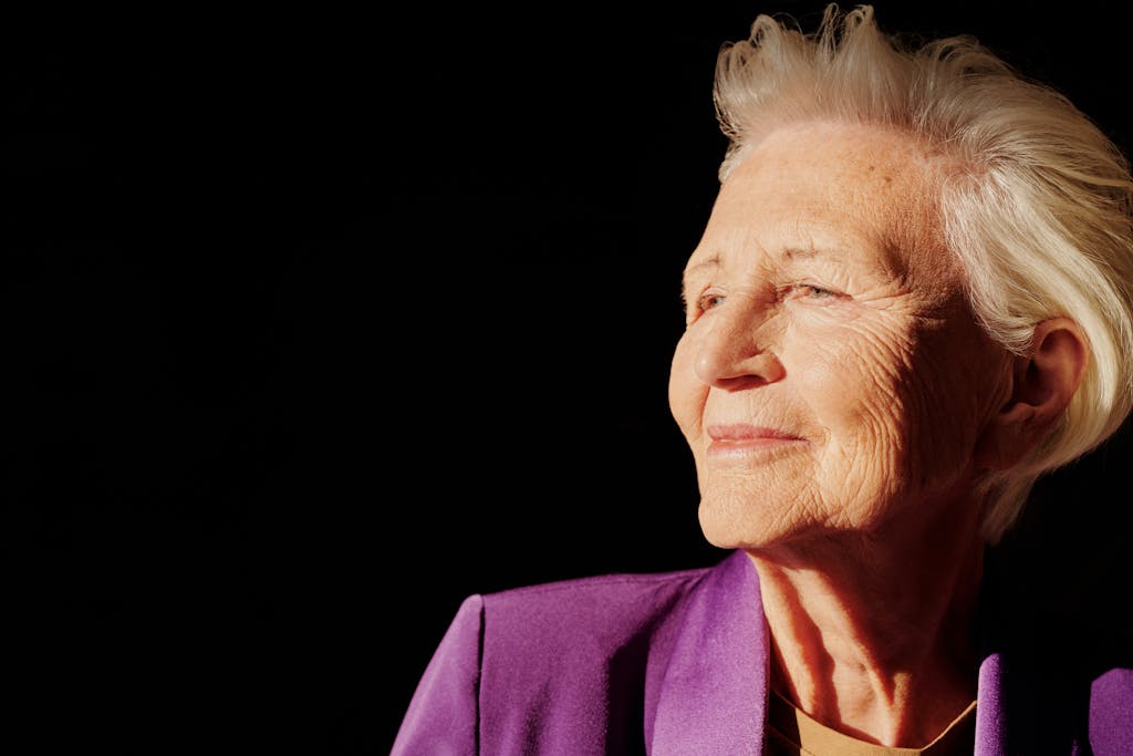 Elegant senior woman smiling with confidence in a purple jacket against black background.