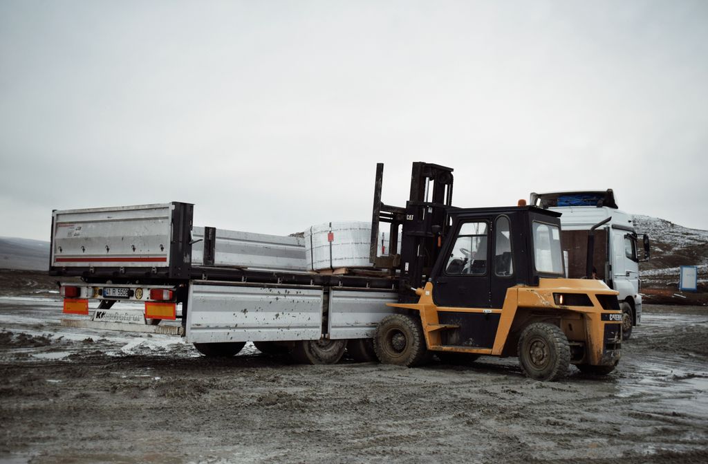 Forklift loading materials onto a truck in an industrial landscape.
