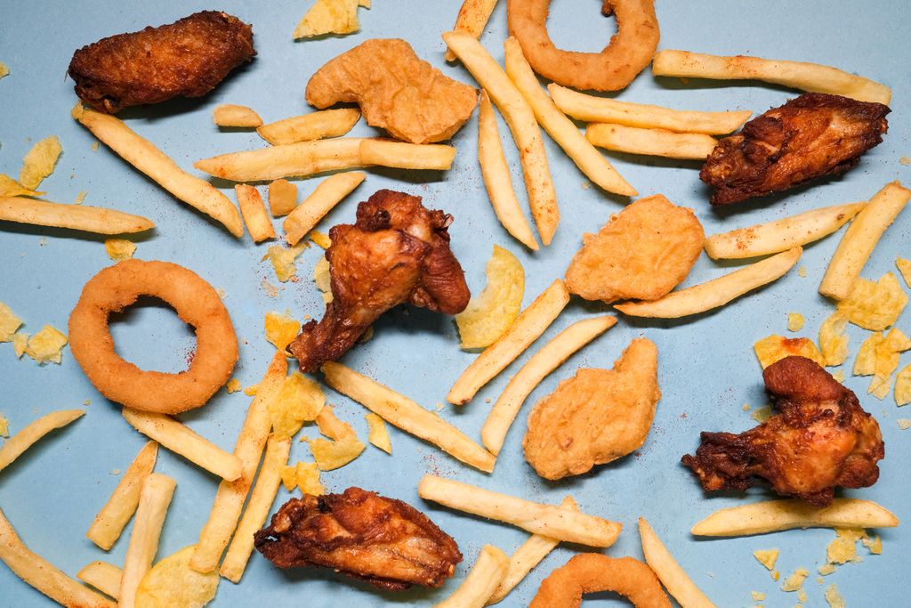 From above of french fries and grilled chicken wings with golden deep fried onion rings and nuggets with chips on blue background in bright studio