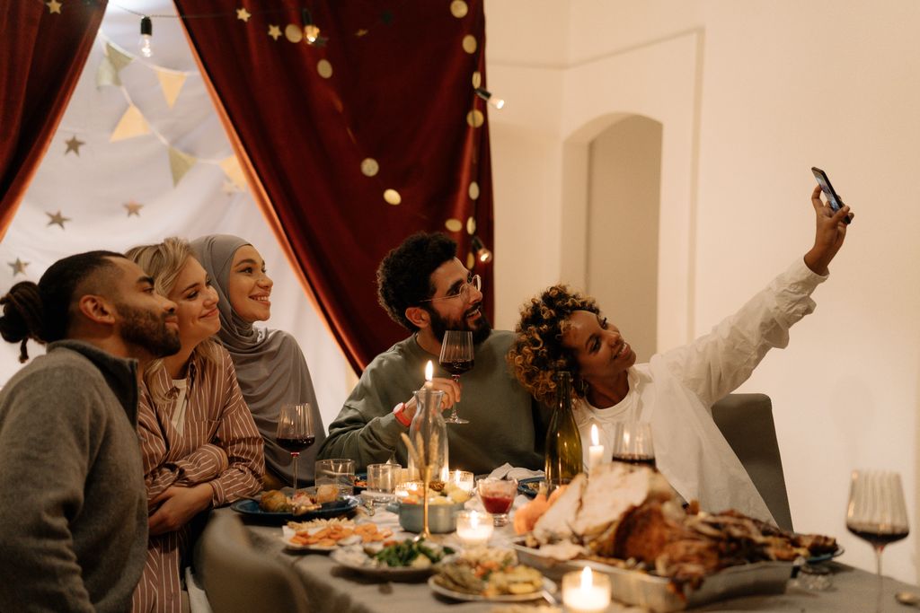 Group of diverse friends enjoying a festive meal indoors and capturing the moment with a selfie.