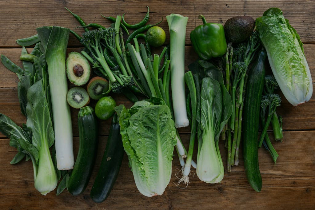 High-angle view of assorted fresh green vegetables arranged on a wooden table.