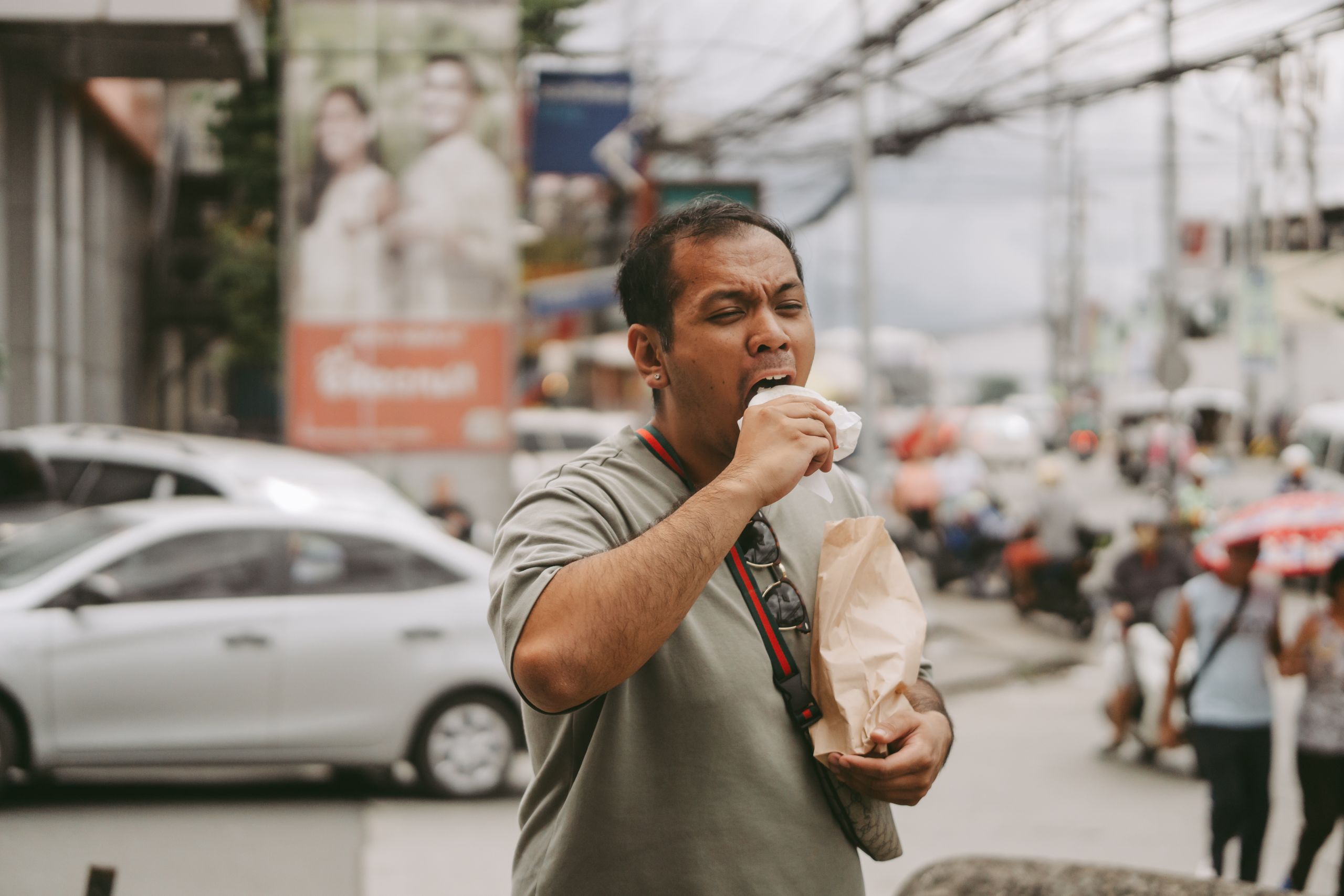 Man enjoying street food amidst a busy city scene with cars and pedestrians.