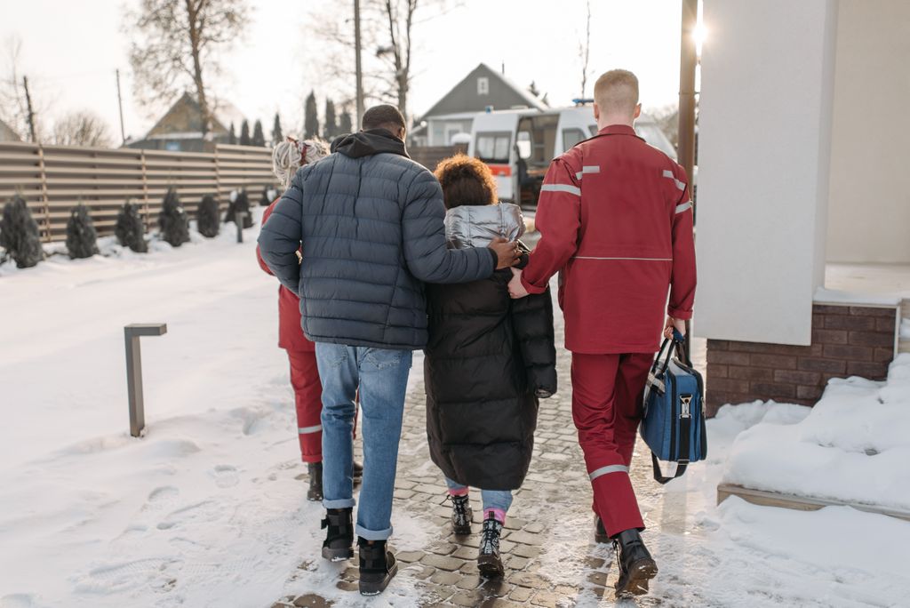 Paramedics assist people on a snowy street towards an ambulance in winter.