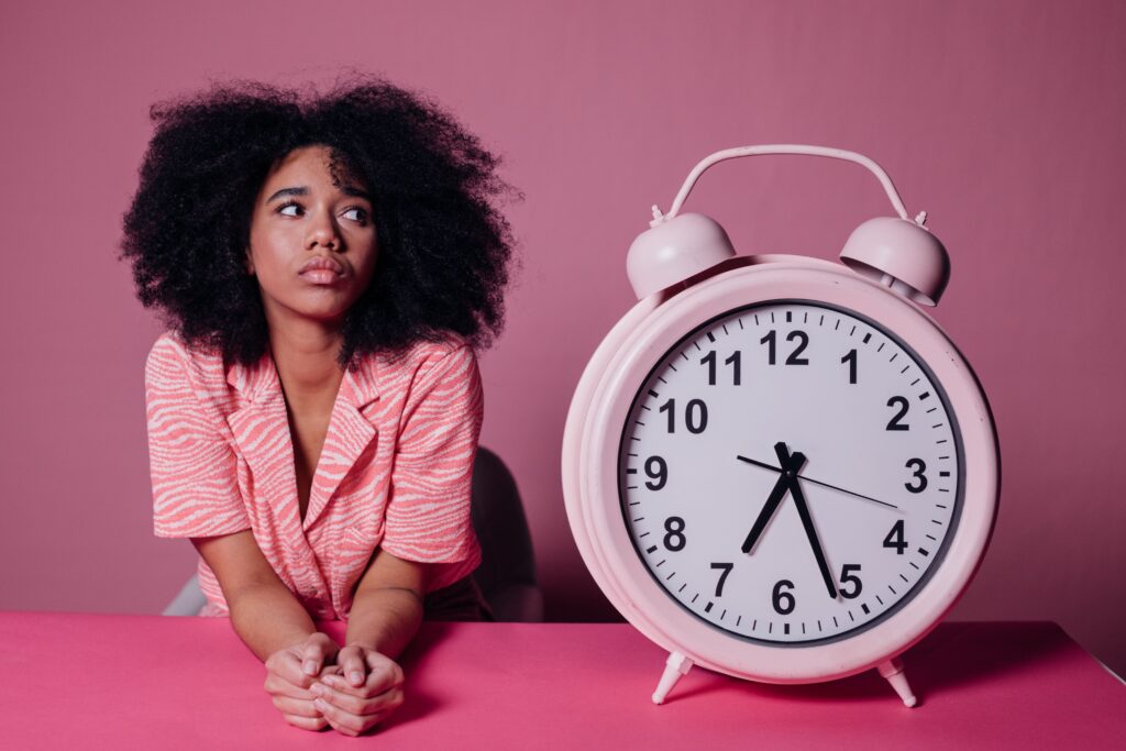 woman-in-pink-long-sleeve-shirt-sitting-beside-white-and-pink-alarm-clock