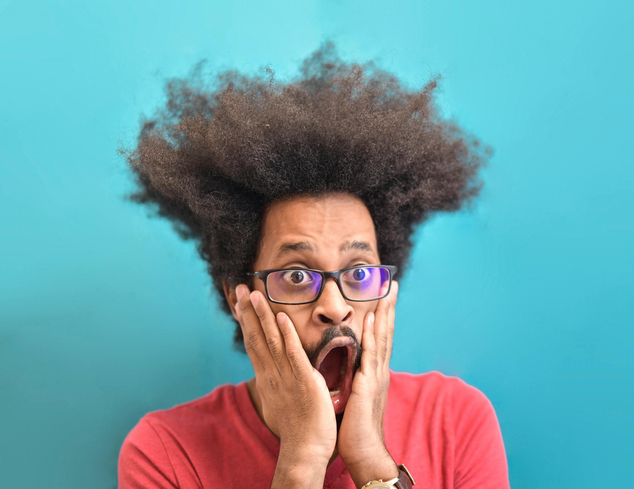 Portrait of a surprised man with an afro hairstyle and eyeglasses against a bright background.