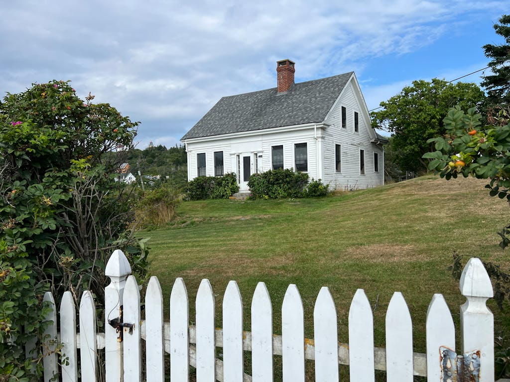 Quaint white cottage with picket fence and lush garden, perfect for a serene coastal retreat.