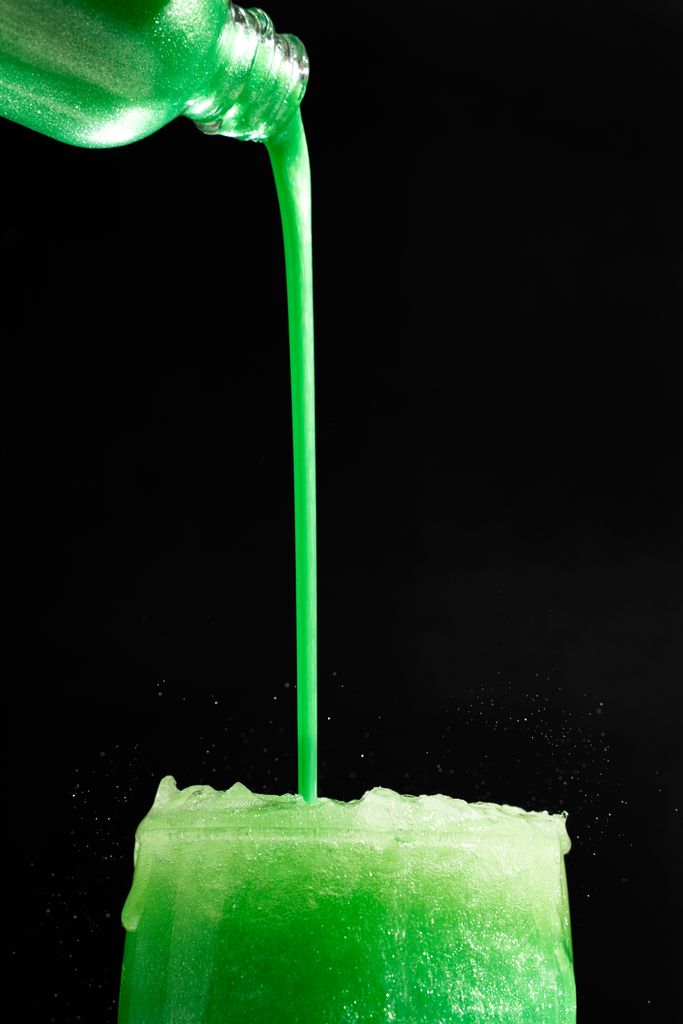 Refreshing green drink pouring into a glass with sparkling edible glitter on a black background.