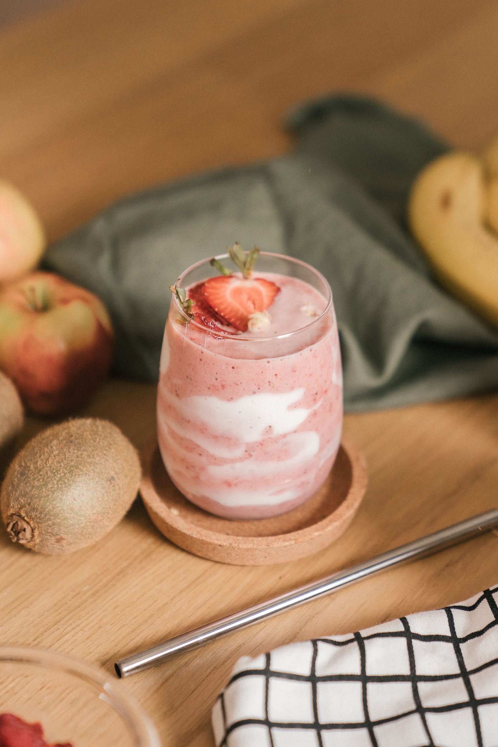 Refreshing strawberry kiwi smoothie in clear glass with fresh fruits on wooden table.