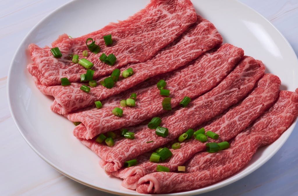 Slices of marbled Wagyu beef arranged on a plate with green onion garnish, ideal for gourmet cooking.