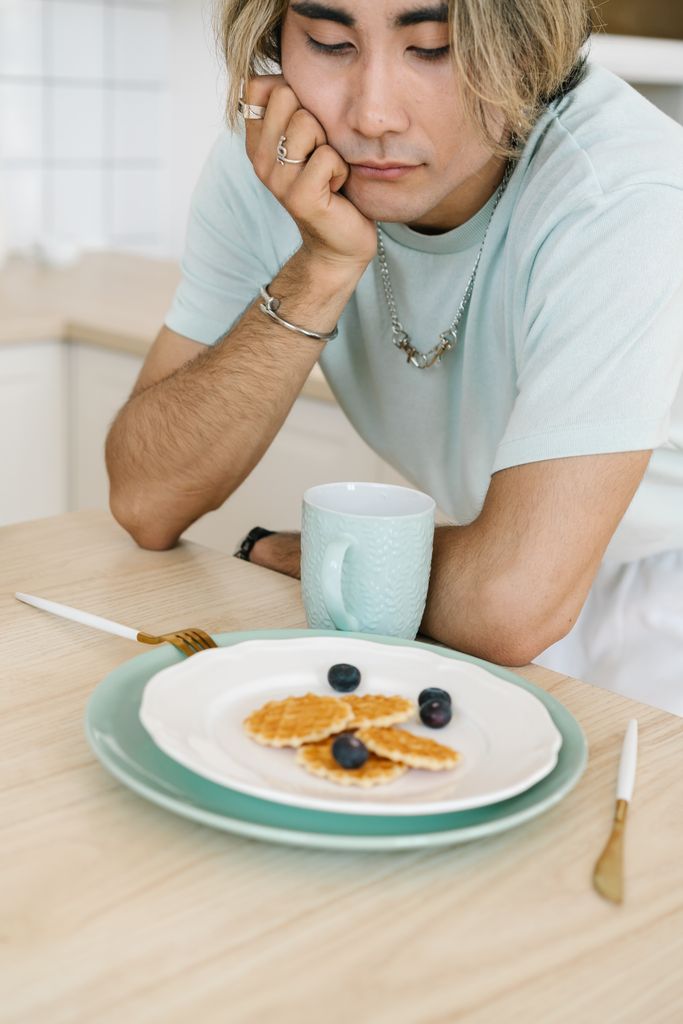 Thoughtful man in kitchen with waffles and blueberries on a plate, creating a pensive mood.