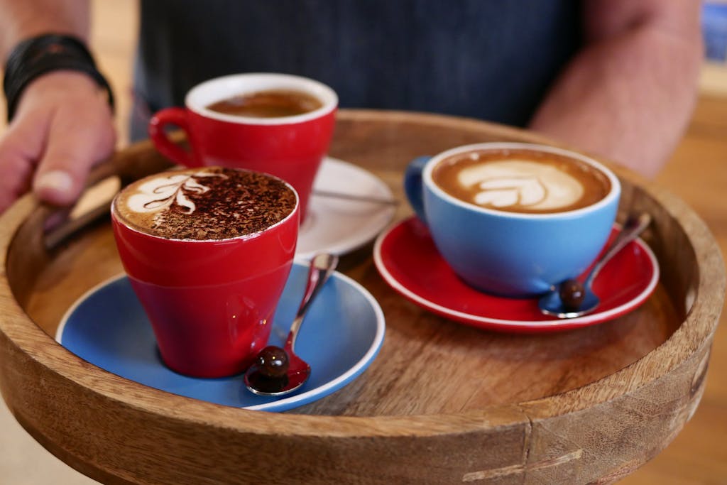 Three colorful cups of coffee with latte art on a round wooden tray, perfect for coffee lovers.