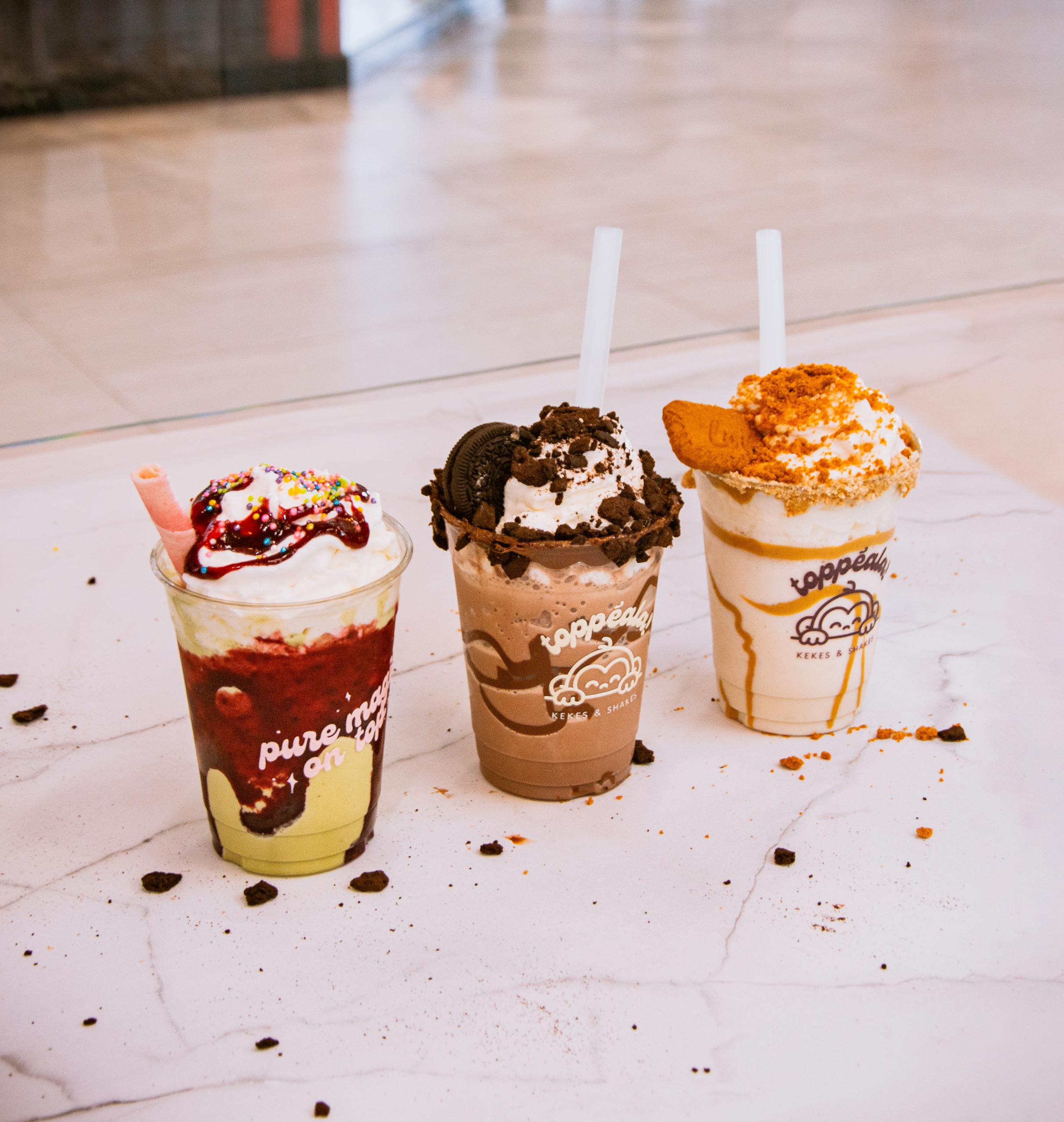 Three colorful milkshakes topped with whipped cream on a marble surface, perfect for dessert inspiration.