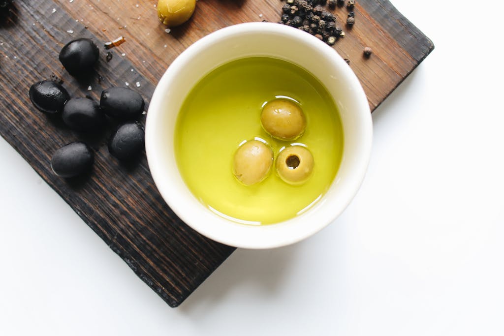 Top view of green olives in oil, black olives, and pepper on a cutting board.
