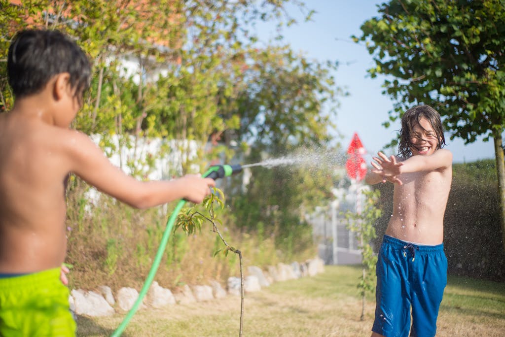 Two boys enjoying a playful water hose fight in a sunny backyard.