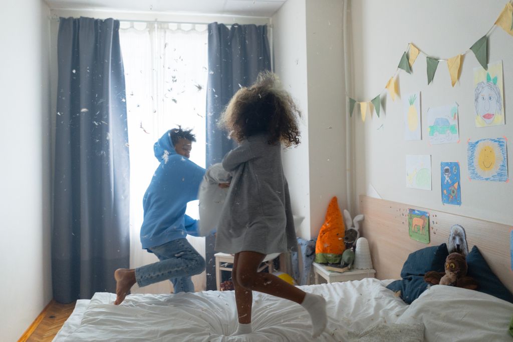 Two children having fun with a pillow fight in a cozy bedroom setting, creating a joyful and playful atmosphere.