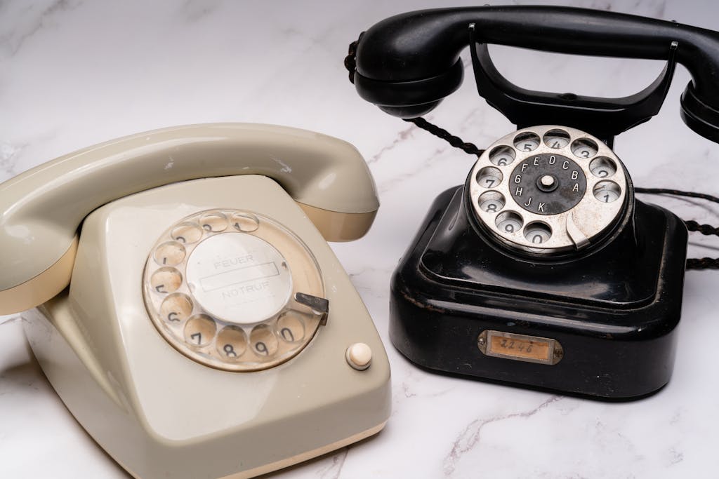 Two classic rotary dial telephones, one black and one beige, on a marble surface.