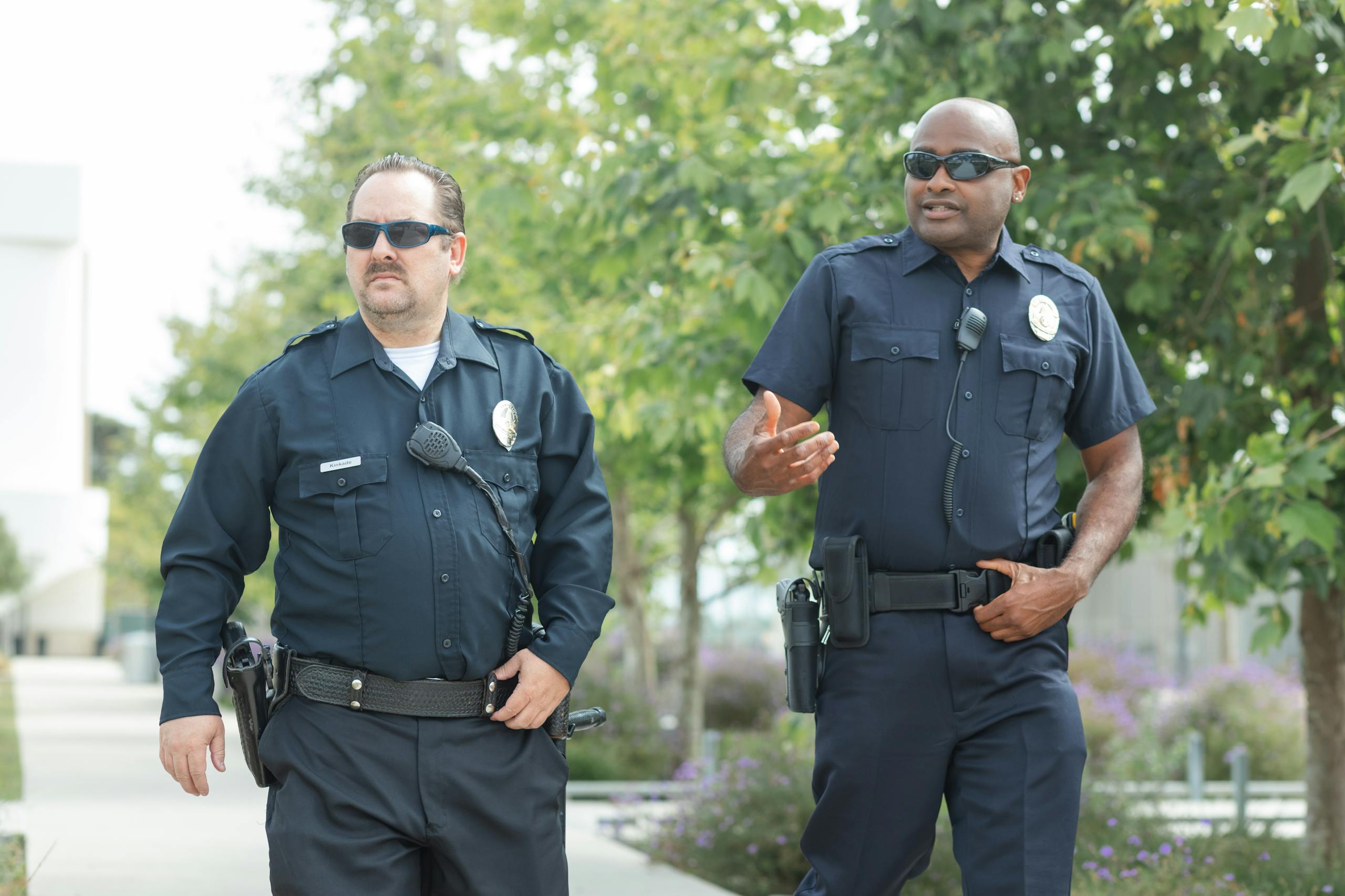 Two police officers walking outdoors, wearing uniforms and sunglasses, engaged in conversation.