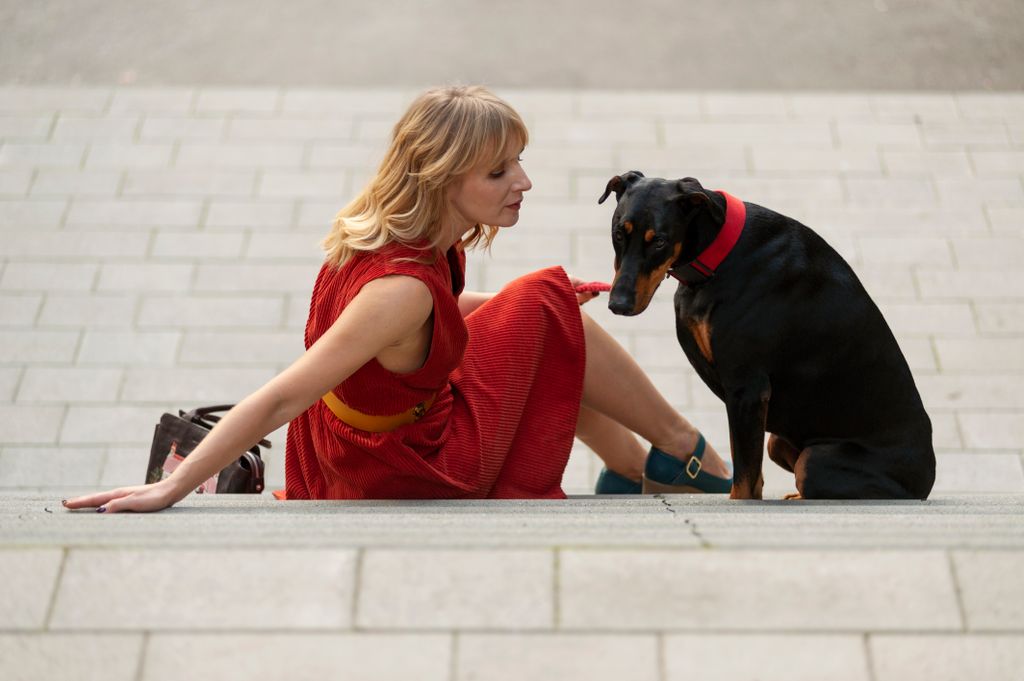 Woman in red dress and Doberman sitting on stairs in urban setting. Captivating moment outdoors.